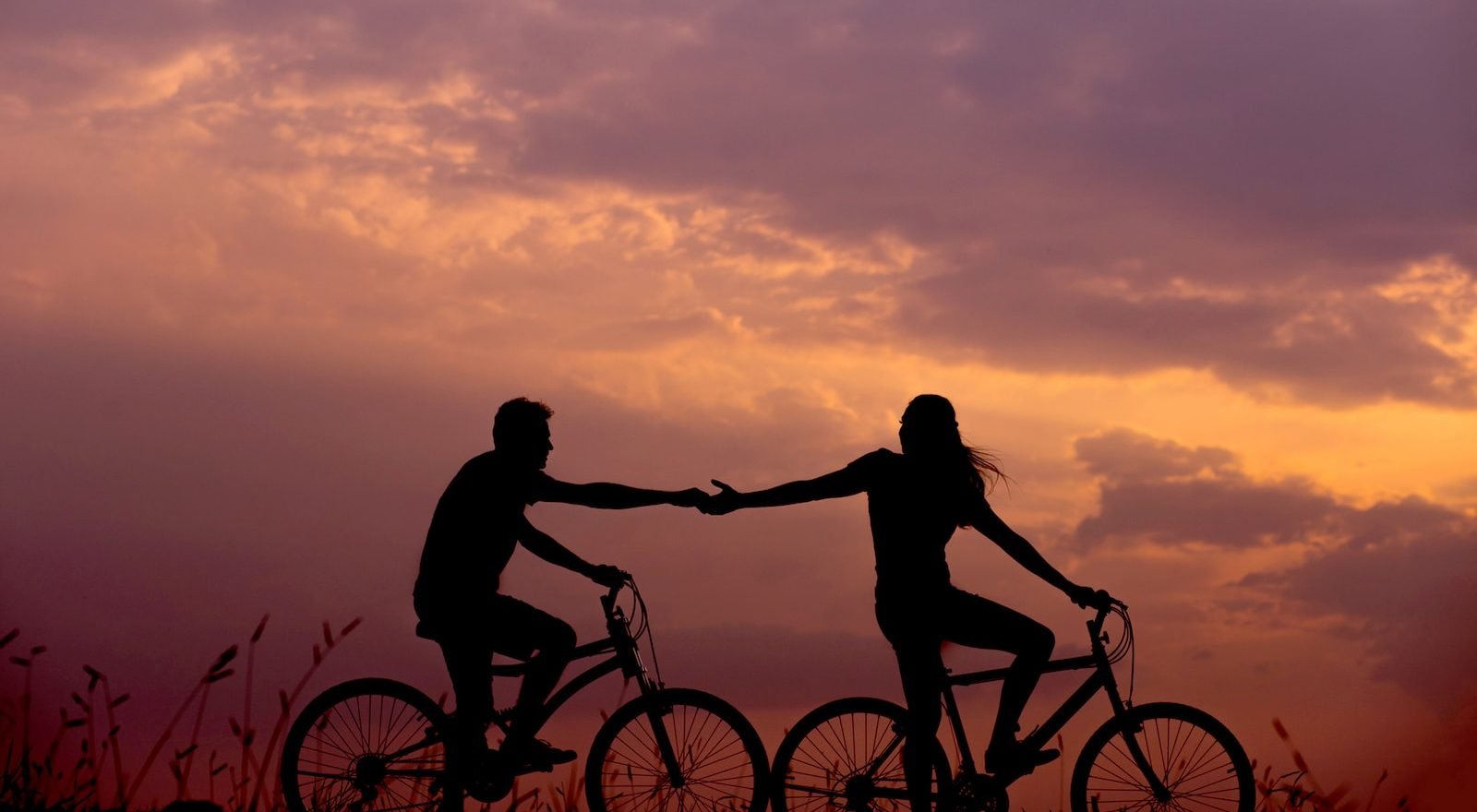 woman on bike reaching for man's hand behind her also on bike