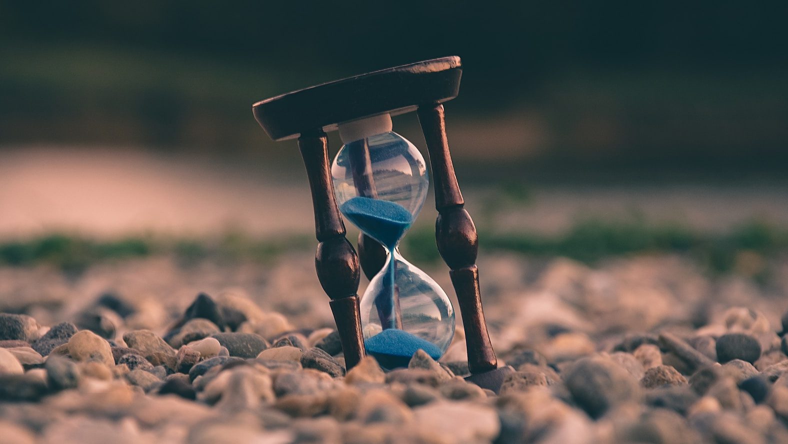selective focus photo of brown and blue hourglass on stones